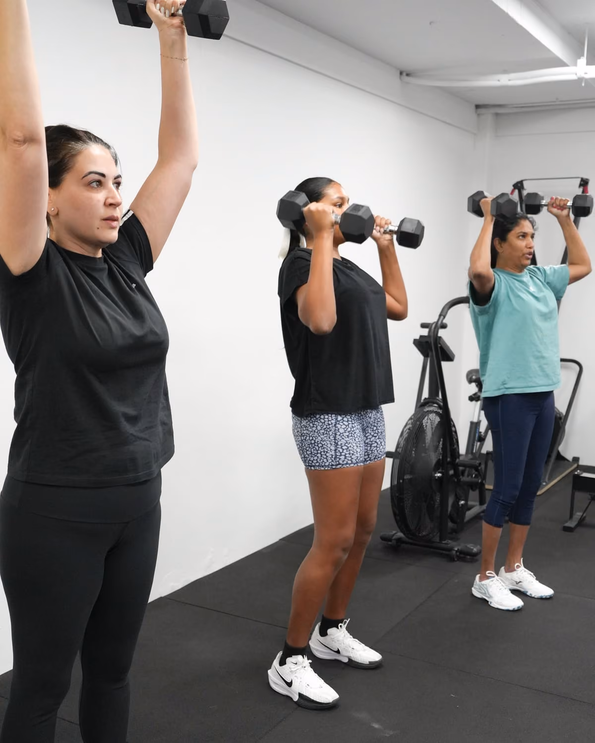Members working through a standing dumbbell press in the strength and conditioning space