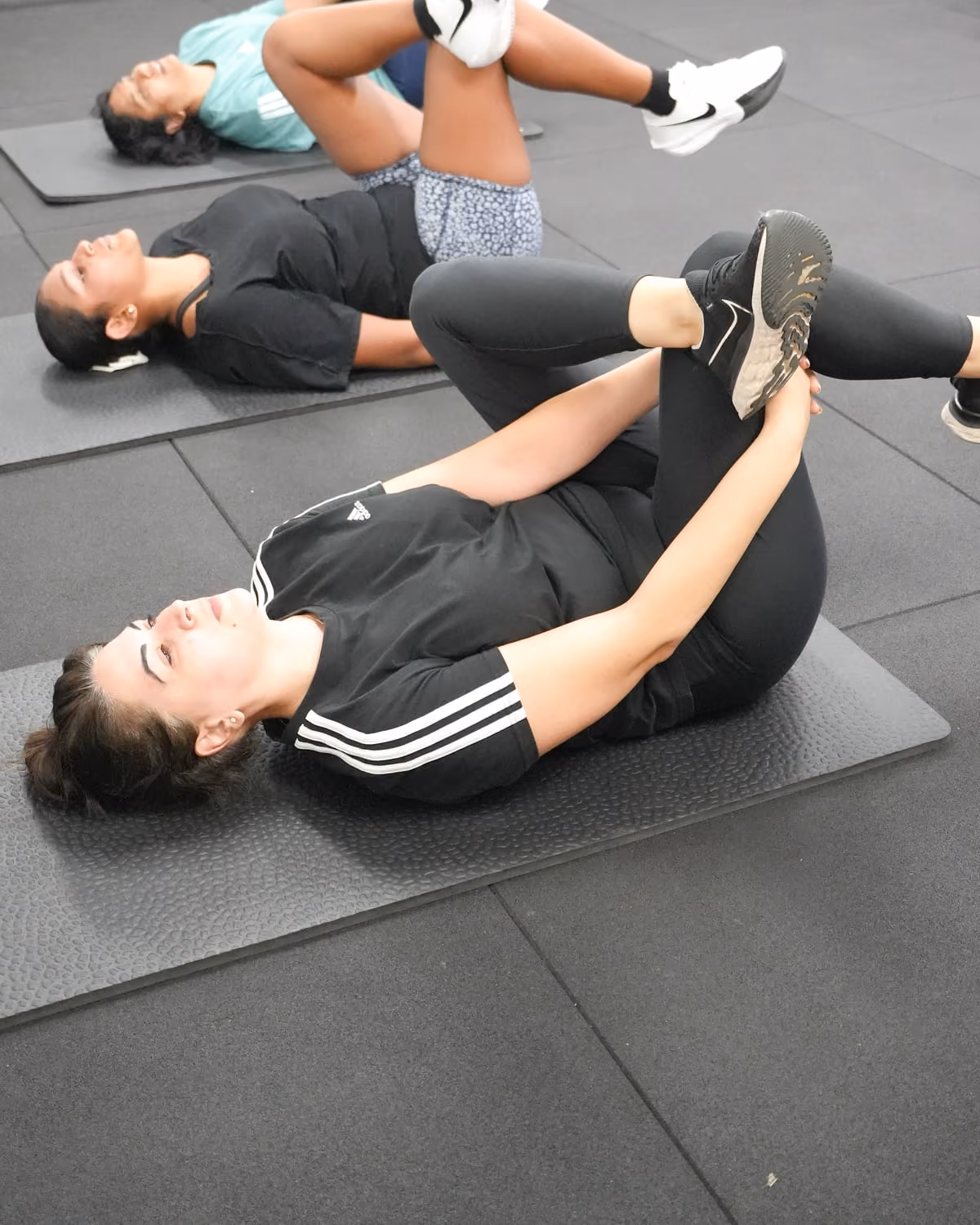 Three members on their mats, each drawing one knee towards the chest with the other leg extended