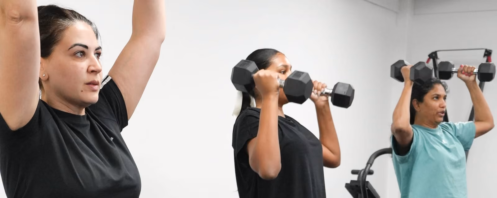 Members pressing dumbbells overhead during a strength class