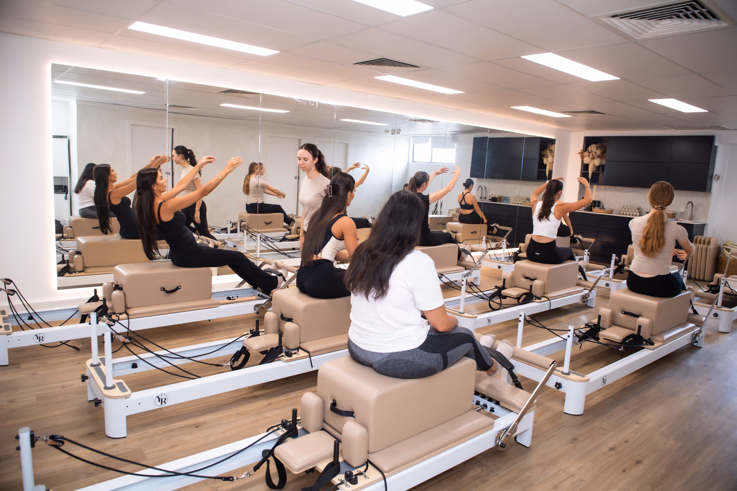 Women seated with arms extended during a group reformer Pilates class