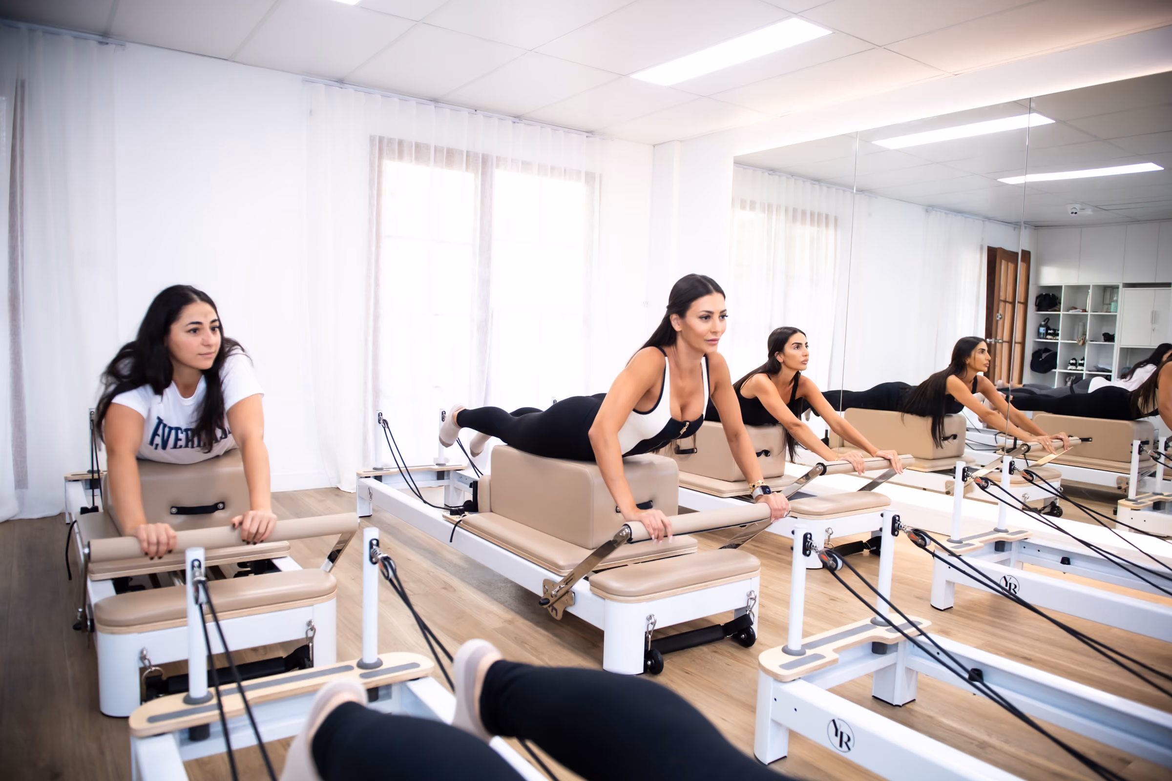 Clients performing prone reformer work beside the studio’s curtained windows