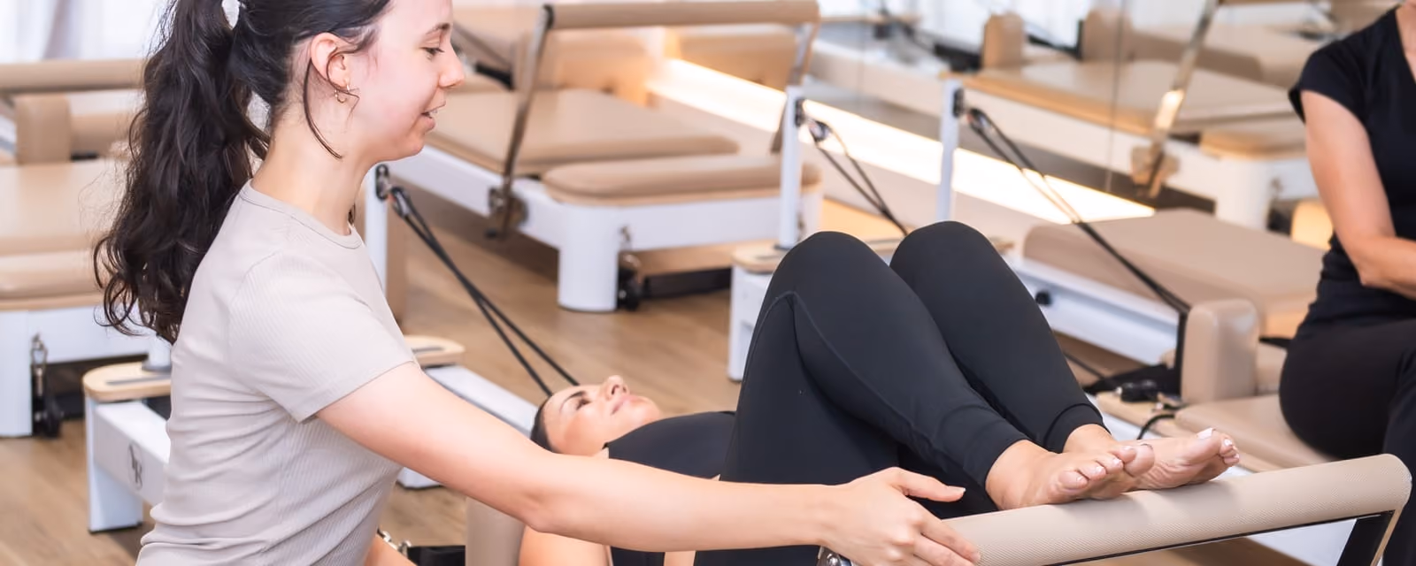 Instructor supporting a member through a reformer strength exercise